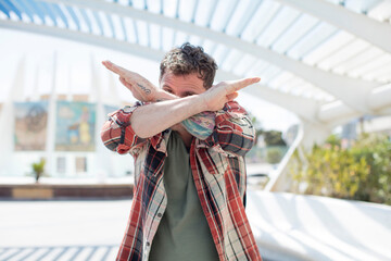 handsome man covering face with hand and putting other hand up front to stop camera, refusing...