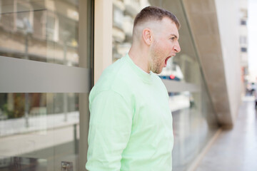 Obraz premium handsome man shouting aggressively, looking very angry, frustrated, outraged or annoyed, screaming no