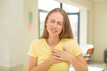 pretty blond woman looking sad, hurt and heartbroken, holding both hands close to heart, crying and feeling depressed