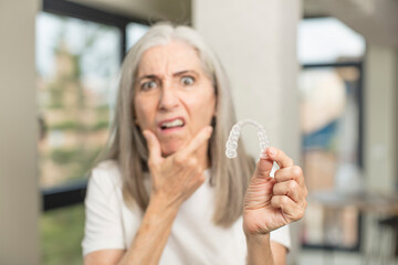 pretty senior woman with mouth and eyes wide open and hand on chin. with a dental retainer