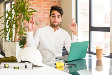 young hispanic man crossing fingers anxiously and hoping for good luck with a worried look....