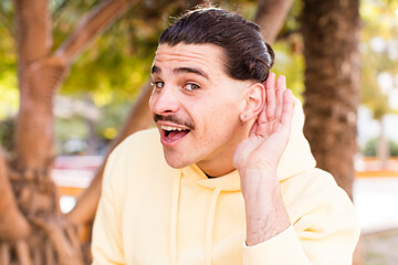 young cool man looking happy, listening, trying to hear a secret conversation or gossip, eavesdropping