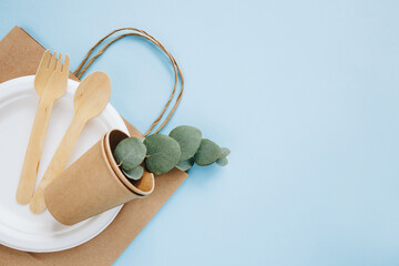 Eco-friendly disposable utensils made with wood and paper on a blue background. Spoons, fork, knives, bowls with paper cups and packet