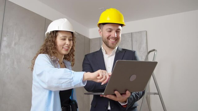 young man and woman in helmet choose room design on computer during an indoor renovation