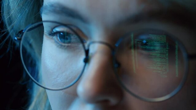 Extreme close up of woman sitting at desk coding in computer program wearing glasses with reflection of screen
