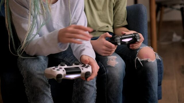 kids hands with joysticks, two children siblings playing video game console while sitting at home, real people, leisure concept.