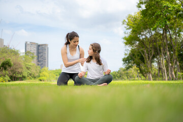 Fototapeta premium Young female and little girl with outdoor activities in the city park, Yoga is her chosen activity.