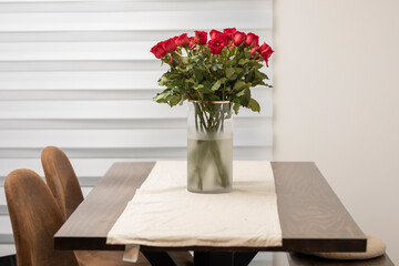 A vase with roses on the table with chairs on the sides