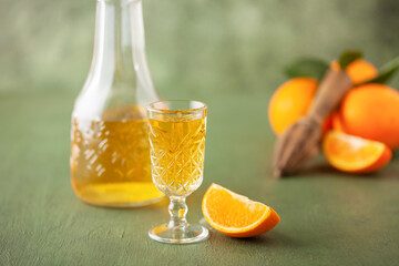 Arancello in grappas wineglass, sweet Italian orange liqueur, traditional strong alcoholic drink and oranges on the green wooden background.
