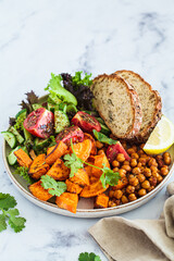 Vegan lunch plate: vegetable salad, fried chickpeas and baked sweet potato with healthy bread. Healthy vegan diet concept.