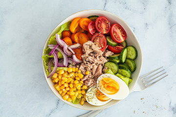 Tuna salad with egg, tomato, cucumber, onion and corn in white bowl, white background.