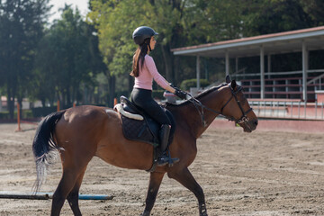 Side shot of a young woman riding a horse in an equestrian center