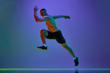 Competitive, motivated man, professional runner, sportsman in motion, training shirtless against blue studio background in neon light
