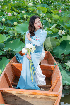 Vietnamese woman wearing Ao dai costume sitting on a boat in a lotus pond.