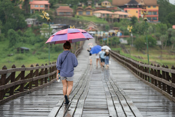 Asian woman walking alone with an umbrella on a wooden bridge.