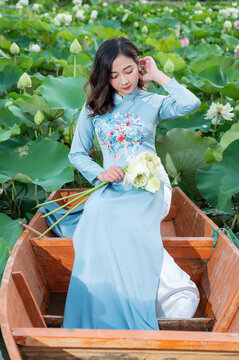 Vietnamese woman wearing Ao dai costume sitting on a boat in a lotus pond.