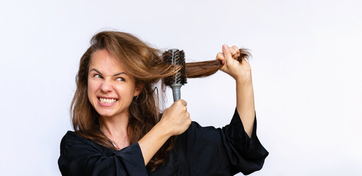 Annoyed angry brunette woman unsuccessfully trying to style her  hair with hair comb.