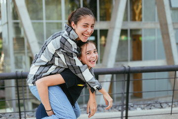 two teenage sisters in the city, one riding on the back of the other, laughing
