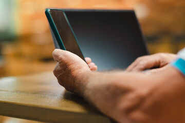 Defocused senior man sitting at bar table using laptop and mobile phone. Mature caucasian man in business work