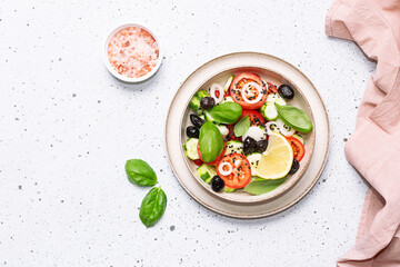 Fresh vegan salad made with tomatoes, olives, cucumbers, onion, basil leaves and seeds in the ceramic bowl on white marble background top view, copy space for your design.