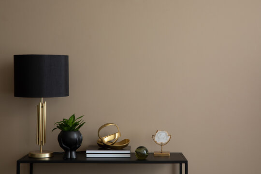 Minimalist composition of cozy living room interior with copy space, black rack, books, gold sculpture, stylish lamp, plant in flowerpot, brown wall and personal accessories. Home decor. Template.