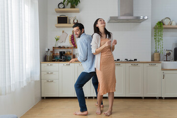 Overjoyed millennial husband and wife dancing in modern kitchen celebrate wedding anniversary at home together, happy young couple tenants have fun enjoy family