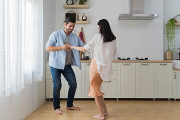 Happy couple having fun in the kitchen dancing together celebrating immigration or anniversary handsome young husband holding hands beautiful wife