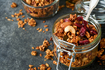 Homemade granola in glass jar with greek yogurt or milk and cashews, almonds, pumpkin with dried cranberry seeds in dark grey table background. Healthy energy breakfast or snack. Top view