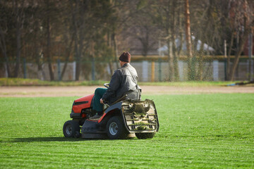 A man on a lawn mower mows the grass. The stadium has been cleared of vegetation. A field for sports games.