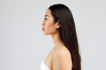 Profile portrait of young chinese lady looking aside at copy space, posing wrapped in towel over gray background