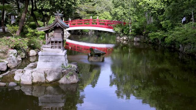 Small shrine and turtle fountain in quiet pond with red bridge at Japanese shrine