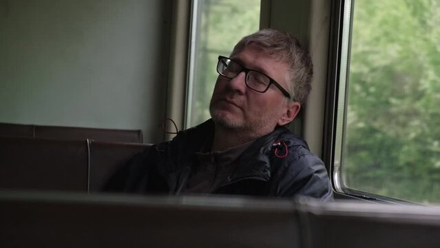 portrait of handsome, unshaven middle aged man dozing off in commuter train carriage by window. tired person is resting on way. transportation of people over long distances by rail. slow motion.