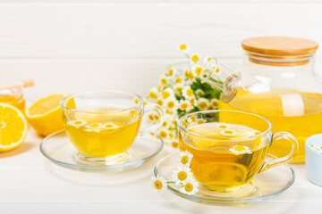 Chamomile herbal tea in a glass cup on a white wooden table with honey, lemon and chamomile bouquet. Close-up. Copy space. Useful herbal drinks, immunity tea. Natural healer concept.Place for text.