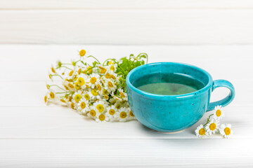 Chamomile herbal tea in a cup on a white wooden table with a bouquet of chamomile. Close-up. Copy space. Useful herbal drinks, immunity tea. Natural healer concept.Place for text.