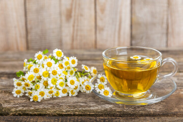 Chamomile herbal tea in a glass cup on a brown wooden table with honey, lemon and chamomile bouquet. Close-up. Copy space. healthy herbal drinks, immunity tea. Natural healer concept.Place for text.