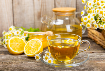 Chamomile herbal tea in a glass cup on a brown wooden table with honey, lemon and chamomile bouquet. Close-up. Copy space. healthy herbal drinks, immunity tea. Natural healer concept.Place for text.