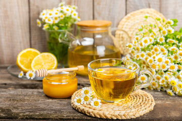 Chamomile herbal tea in a glass cup on a brown wooden table with honey, lemon and chamomile bouquet. Close-up. Copy space. healthy herbal drinks, immunity tea. Natural healer concept.Place for text.