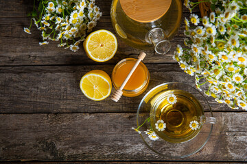 Chamomile herbal tea in a glass cup on a brown wooden table with honey, lemon and chamomile bouquet. Close-up. Copy space. healthy herbal drinks, immunity tea. Natural healer concept.Place for text.