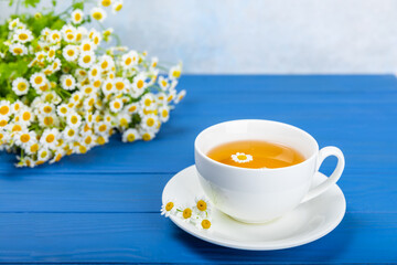 Chamomile herbal tea in a cup on a blue wooden table with honey, lemon and chamomile bouquet. Close-up. Copy space. healthy herbal drinks, immunity tea. Natural healer concept.Place for text.