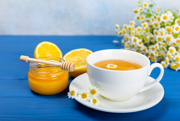 Chamomile herbal tea in a cup on a blue wooden table with honey, lemon and chamomile bouquet. Close-up. Copy space. healthy herbal drinks, immunity tea. Natural healer concept.Place for text.