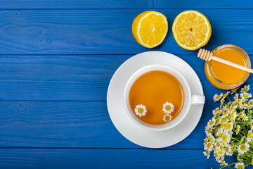 Obraz na płótnie Canvas Chamomile herbal tea in a cup on a blue wooden table with honey, lemon and chamomile bouquet. Close-up. Copy space. healthy herbal drinks, immunity tea. Natural healer concept.Place for text.