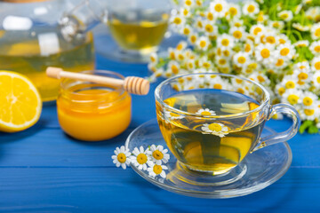Chamomile herbal tea in a cup on a blue wooden table with honey, lemon and chamomile bouquet. Close-up. Copy space. healthy herbal drinks, immunity tea. Natural healer concept.Place for text.