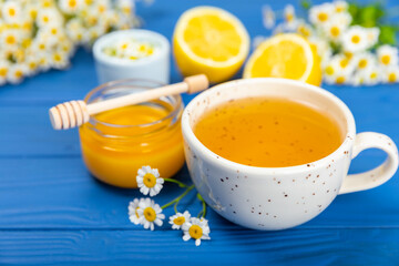 Chamomile herbal tea in a cup on a blue wooden table with honey, lemon and chamomile bouquet. Close-up. Copy space. healthy herbal drinks, immunity tea. Natural healer concept.Place for text.