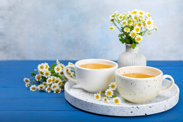 Chamomile herbal tea in a cup on a blue wooden table with honey, lemon and chamomile bouquet. Close-up. Copy space. healthy herbal drinks, immunity tea. Natural healer concept.Place for text.
