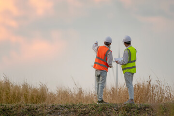 Two Asian engineers or technician men in uniform discuss and checking. Wind turbines ecological energy industry power windmill field worker renewable background.