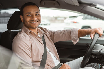 Joyful indian man driving car smiling at camera sitting inside