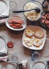 Mesa de comida familiar con platos, vasos, servilletas, bebidas y comida ya lista para empezar a comer.