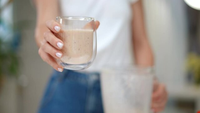 Unrecognizable woman stretching glass with tasty smoothie in slow motion to camera. Front view young Caucasian lady showing delicious cocktail standing indoors