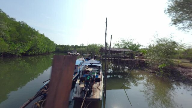 Aerial low dynamic view flying over calm river surface between green trees forest with village harbor port Asian fishing boat. FPV sport drone shot tropical pond rustic house nature lush vegetation 4k