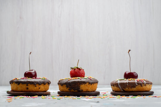 a front view little chocolate donuts with designed fruits on top on the grey background sweet sugar cake fruit chocolate